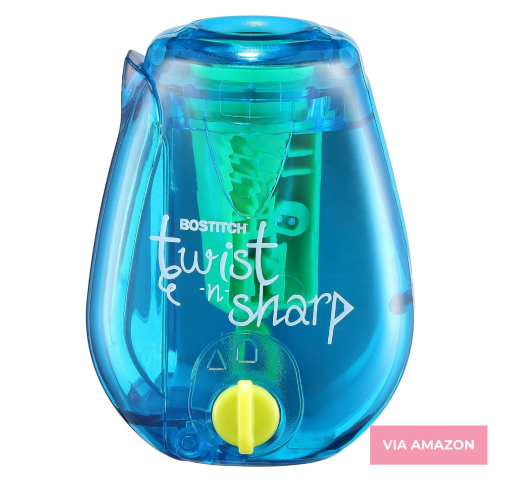 Blue Bostitch Twist-n-Sharp manual pencil sharpener with a transparent body, green blade mechanism, and a yellow twist dial at the bottom. The image has a "Via Amazon" tag in the bottom right corner.