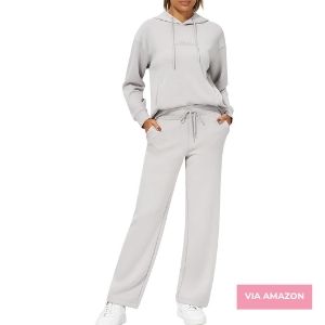 Person wearing a light gray hooded sweatshirt and matching drawstring pants, standing with hands in pockets. "VIA AMAZON" text in bottom right corner.