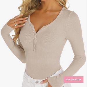 Woman wearing a fitted, beige long-sleeve henley top with button details and white pants, shown from neck to hips.
